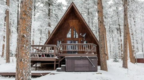 A cozy A-frame cabin surrounded by snow-covered trees in a winter landscape.
