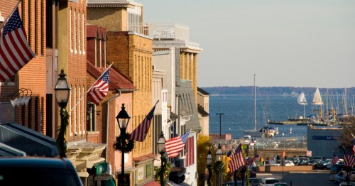 Downtown Annapolis, MD on a summer day, showing brick buildings waving American flags and the waterfront under a blue sky.