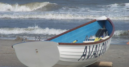 A small boat with "Avalon" painted on it, set against the backdrop of a New Jersey shorefront.