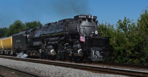 Big Boy No. 4014, the world's largest steam locomotive, travels on tracks next to green trees and with blue sky above.
