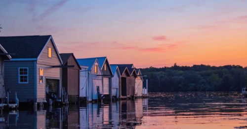 A row of boathouses on the waters of Lake Canandaigua, set against the sunset.