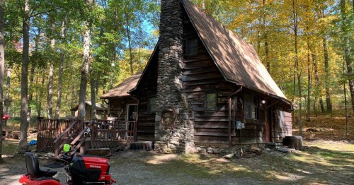 A historic wood and stone cabin located in the woods of Pennsylvania, with an ATV parked in front.