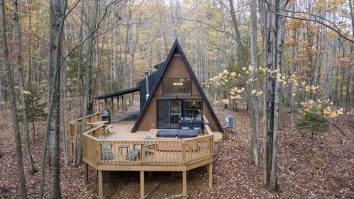 A cozy A-frame cabin surrounded by autumn trees, featuring a wooden deck and outdoor seating.