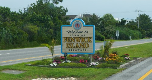 A two-lane highway with a sign in the middle reading "Welcome to Fenwick Island".