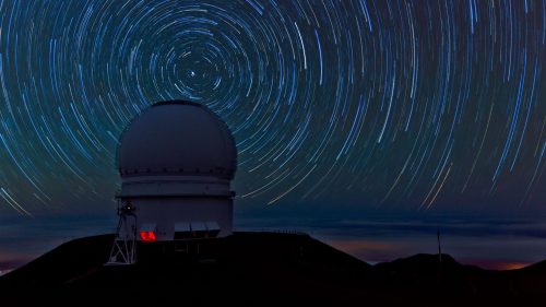 A telescope dome on a mountain under a starry sky, with star trails creating circular patterns around the North Star.