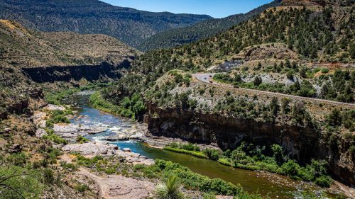 A scenic view of a winding river surrounded by rocky cliffs and lush greenery under a clear blue sky.