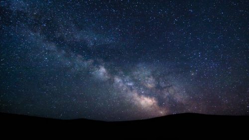 A stunning night sky filled with stars and the Milky Way, silhouetted against dark hills.