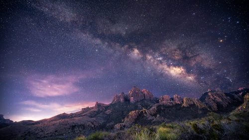 A stunning night sky filled with stars and the Milky Way over rugged mountain peaks.
