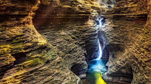 A stunning canyon with layered rock formations and a waterfall cascading into a serene blue pool below.