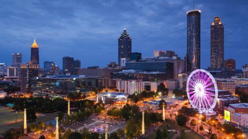 Atlanta skyline at dusk, featuring tall buildings, a Ferris wheel, and illuminated parks.