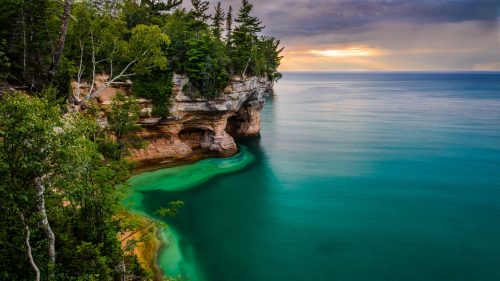 A serene coastal scene with turquoise waters, rocky cliffs, and lush greenery under a cloudy sky.