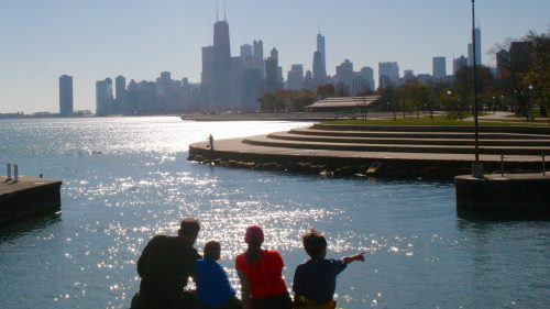 A family sits by the water, overlooking a sparkling Chicago skyline on a sunny day.