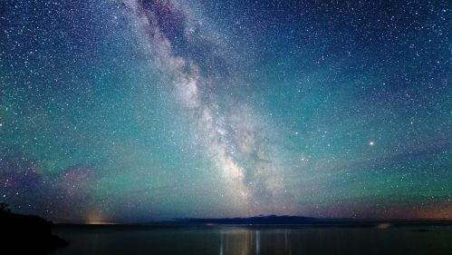 A stunning night sky filled with stars and the Milky Way, reflecting on calm water below.