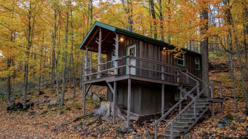 A cozy wooden cabin surrounded by vibrant autumn trees and fallen leaves.