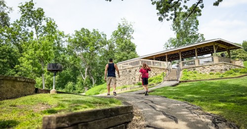 A man and child walking a paved path towards a picnic pavillion, a hidden spot in Gramercy Park, Illinois