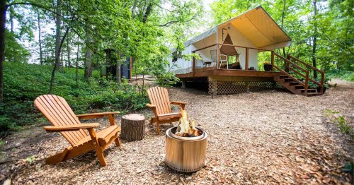 A canvas glamping tent in the woods with a smokeless firepit and Andirondack chairs, a unique glampground in Iowa, near Des Moines.