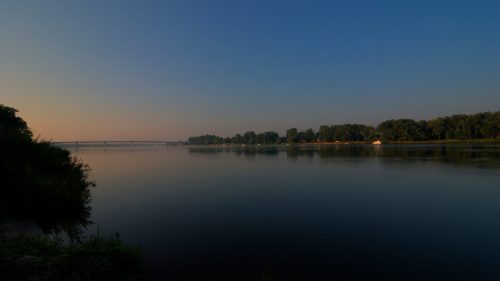 A tranquil river scene at dusk, with calm waters reflecting the sky and trees along the shore.