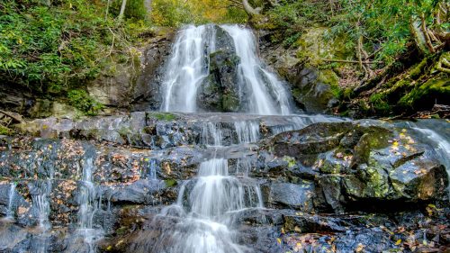 A serene waterfall cascading over rocky terrain, surrounded by lush greenery and autumn foliage.