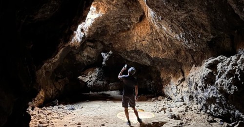 A man looks up at light streaming through a hole in a lava tube in Southern California.