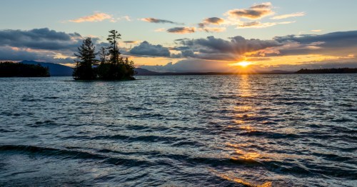 A sunset view of Lily Bay at sunset, from Lily Bay State Park in Maine, with a small island in the water.