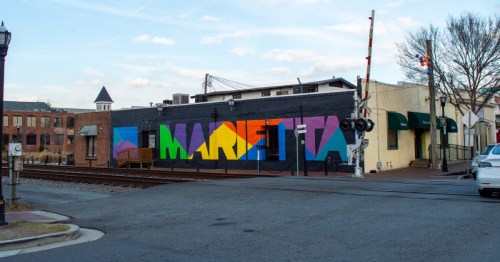 A small-town street, with a rainbow mural reading "Marietta" printed on the side of a building.