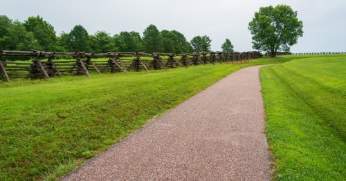 An asphalt path followinq a historic wooden fence at Wilson's Creek National Battlefield, a hidden gem in the Missouri Ozarks
