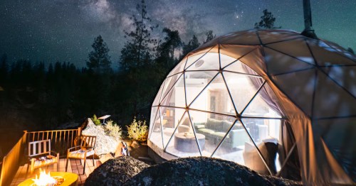 An unexpected dome Airbnb in Garden Valley, Idaho, at night, with bright lights shining inside and the Milky Way overhead.