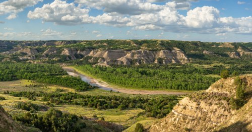 Spring views of Theodore Roosevelt National Park, with green landcapes, golden blufs, and a river. The best nature trails in North Dakota for seeing spring wildflowers are found here.