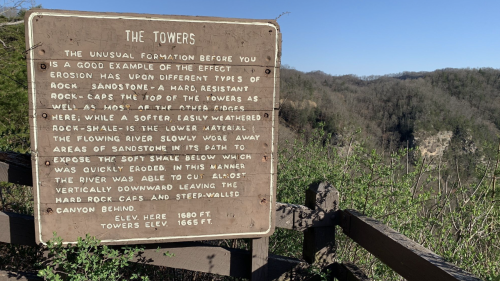 Sign describing "The Towers," a geological formation shaped by erosion, with a canyon visible in the background.