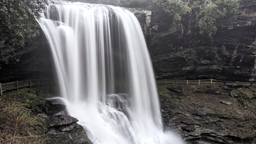 A cascading waterfall flows over rocky cliffs, surrounded by lush greenery and mist.