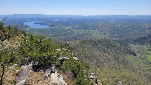 A panoramic view of lush green mountains and a lake under a clear blue sky.