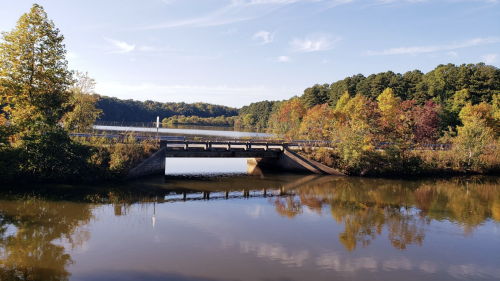 A serene river scene with a bridge, surrounded by colorful autumn trees and a clear blue sky.