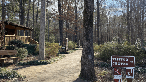 Pathway leading to a visitor center in a wooded area, with signs for biking and walking trails.