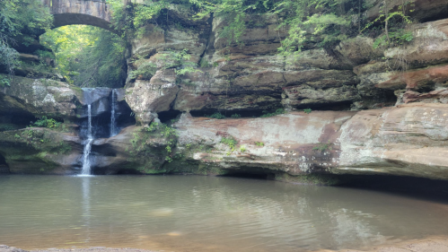 A serene natural scene featuring a small waterfall cascading into a calm pool surrounded by rocky cliffs and greenery.