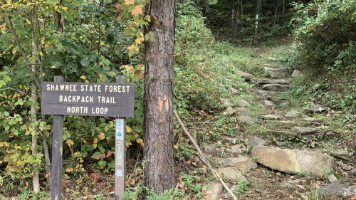 Sign for Shawnee State Forest Backpack Trail North Loop, with a rocky path and surrounding greenery.