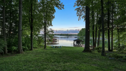 A serene lakeside view framed by trees, with a dock and calm water under a clear blue sky.