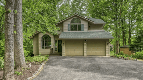 A two-story house surrounded by trees, featuring a double garage and large front windows.