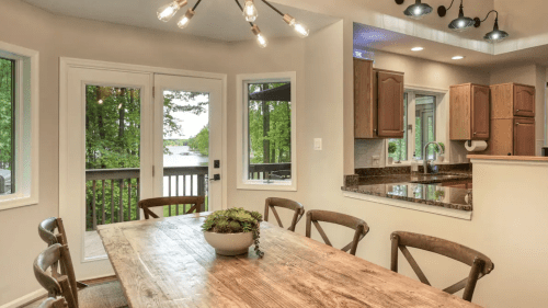 A cozy dining area with a wooden table, surrounded by chairs, and large windows overlooking a scenic view.