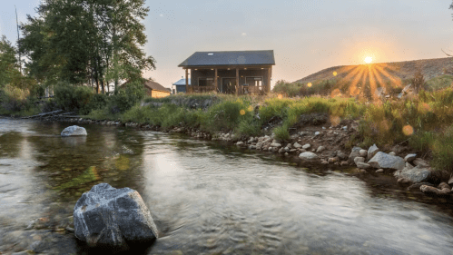 A serene river scene at sunset, with a house in the background and trees lining the shore.