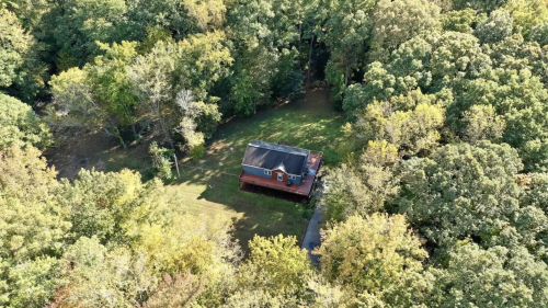Aerial view of a red house surrounded by lush green trees and a grassy yard.