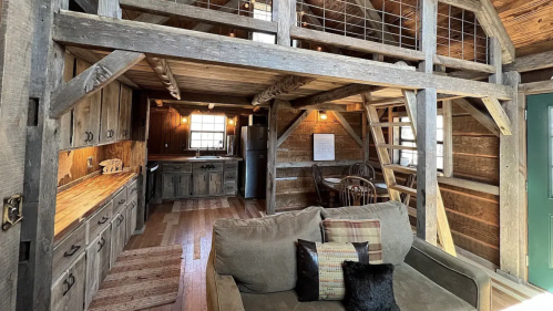 Cozy wooden cabin interior with a loft, kitchen area, and a comfortable sofa. Warm lighting enhances the rustic charm.