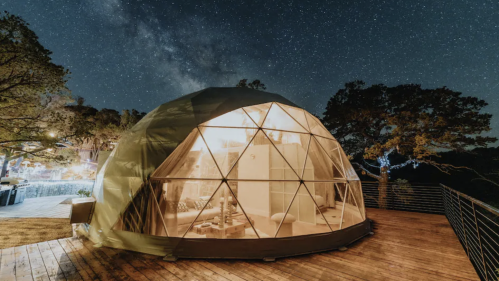 A geodesic dome on a wooden deck under a starry night sky, illuminated from within.