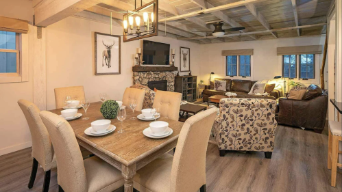Cozy dining area with a wooden table set for six, leading to a living room with a stone fireplace and comfortable seating.