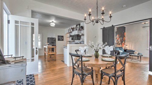 A cozy dining area with a round table set for four, leading to a modern kitchen and living space. Bright and inviting.