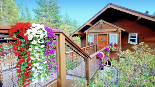 A charming wooden house with vibrant flower arrangements on the railing and a clear blue sky in the background.