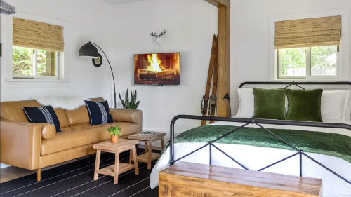 Cozy bedroom with a green bedspread, leather sofa, wooden furniture, and a TV displaying a fireplace.