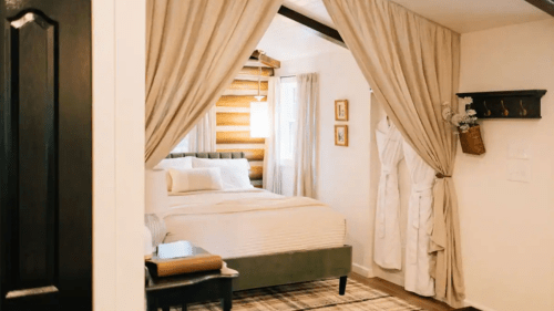 Cozy bedroom with a green bed, draped curtains, and warm wooden accents, featuring a rug and decorative wall art.