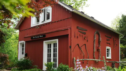 A charming red cottage surrounded by greenery and flowers, featuring rustic decorations on the walls.