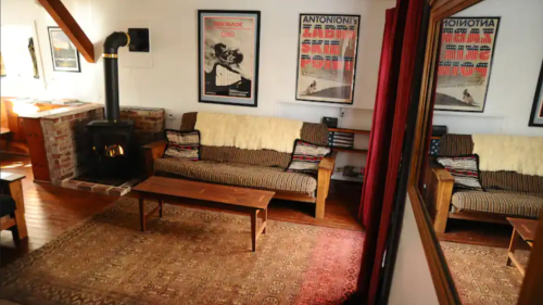 Cozy living room with a wood stove, wooden furniture, and vintage posters on the walls. Warm, inviting atmosphere.