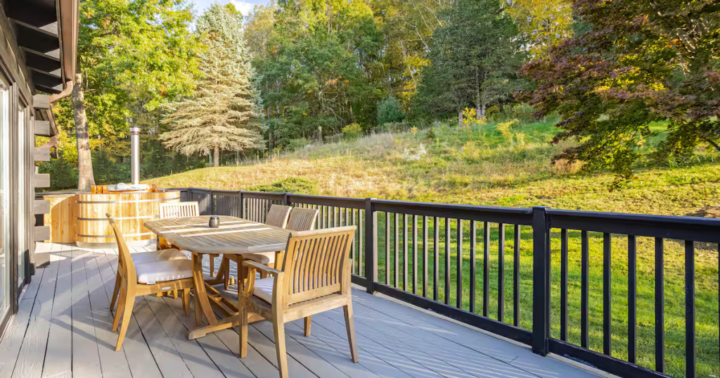 The scenic porch at the Meryall Cabin Airbnb in New Milford, Connecticut features a wooden hot tub and a table and chairs.